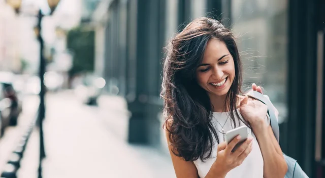 Chica-sonriendo-escribiendo-al-movil-por-la-calla-Happy-woman-texting-on-the-street